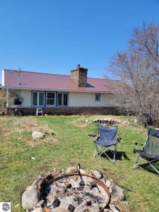 Home on 20 acres in South Boardman has greenhouses, a classic barn, garden areas and a cleared area for livestock or crops. Firepit in foreground is perfect for night-time star gazing at this quiet location.