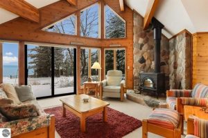 Crystal Drive living room with views of Crystal Lake, stone hearth, view windows, deck and wood walls and ceiling beams.