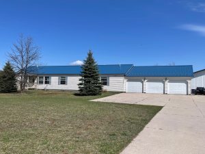 Photo of Leelanau County 10 Acre homestead is a ranch home with a three car garage and evergreen trees in the sunny front yard with concrete driveway.