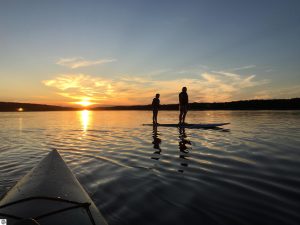 Long Lake Waterfront Home in Benzie County image is of paddleboarders at sunset on Long Lake.