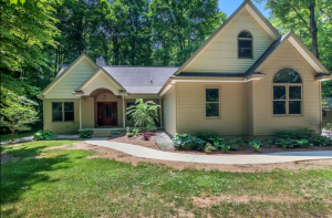 1st Image for FOR SALE southwest of Lake Ann shows a custom home with four peaked roofs, a curved sidewalk to the front door and a backdrop of mature trees with a lawn in the front yard.