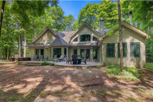 Image 2 for house for sale southwest of Lake Ann shows us the back of the home with numerous large windows and an eyebrow window looking over the backyard deck and hot tub. 