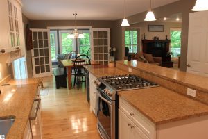 For Sale home near Glen Lake image is taken from one end of the kitchen overlooking the kitchen island and counter into the dining and a corner of the living rooms. The other side of the bar is additional kitchen cabinetry and etc.