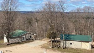 Image for Beulah home on 5 acres shows the home and pole barn from above with a view of lakes in the distance. A driveway separates the two buildings and the mature trees are leafless this time of year.