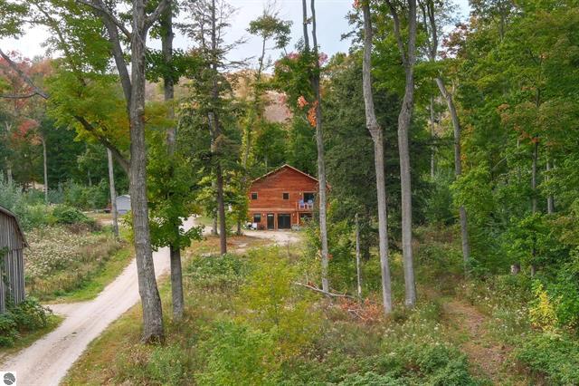 Log cabin at the end of a gravel driveway peeks between mature trees with a tall dune in the background.