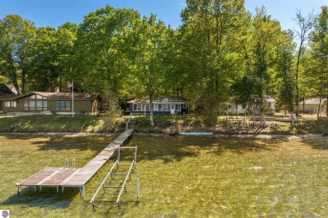 Image for waterfront cottage on Big Platte Lake in Benzie County was taken from the water looking toward the dock and cottage. Windows in the cottage reflect the lake and trees surround it.