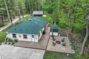 Smart Cabin Retreat photo is an aerial view of the cottage with decking, patio with firepit, storage shed and concrete driveway. Tall trees dot the landscape.