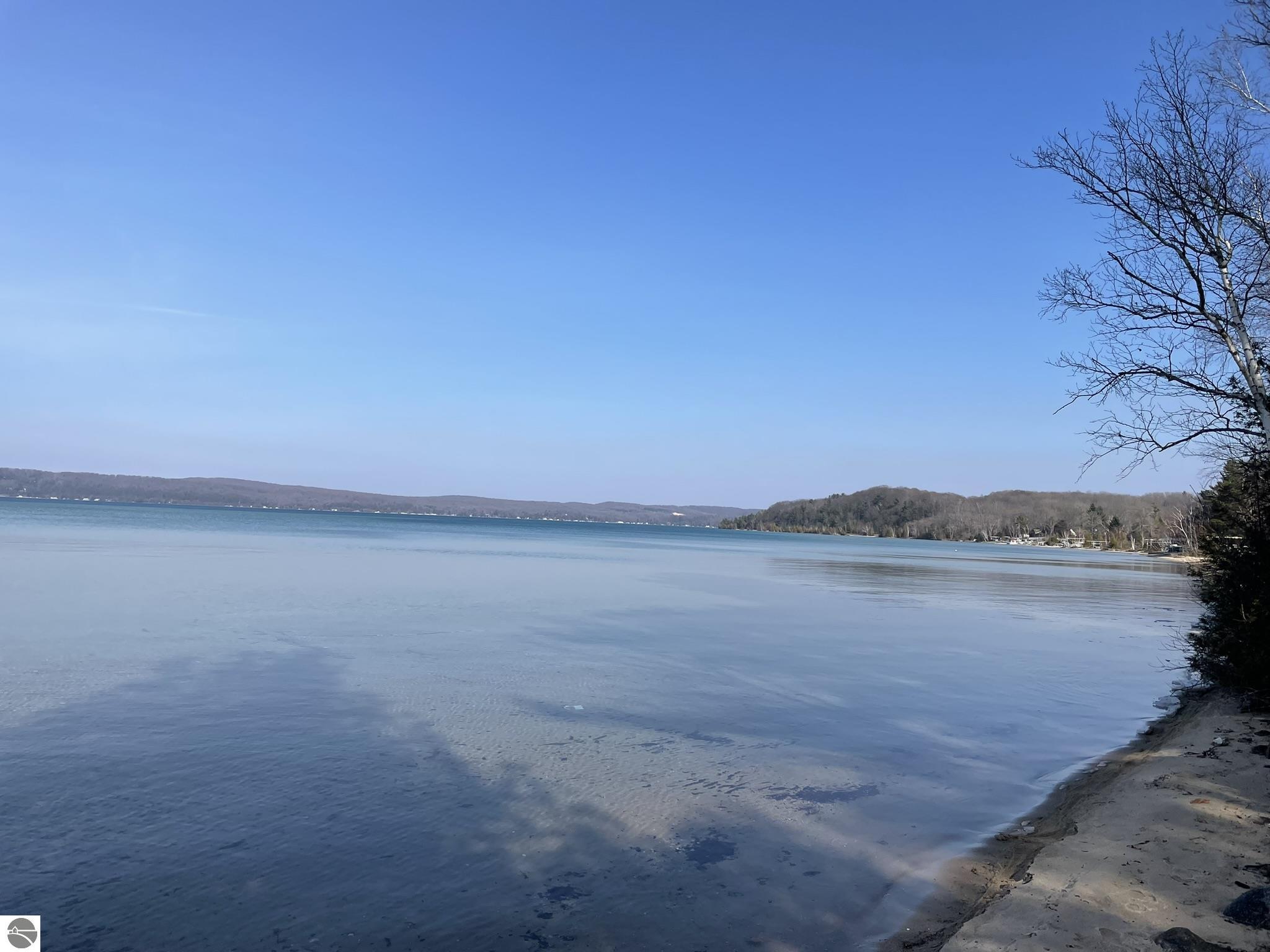 Image of Crystal Lake shared access is of the sandy shoreline, calm lake partially frozen and distant view of wooded hills lining the shore. 