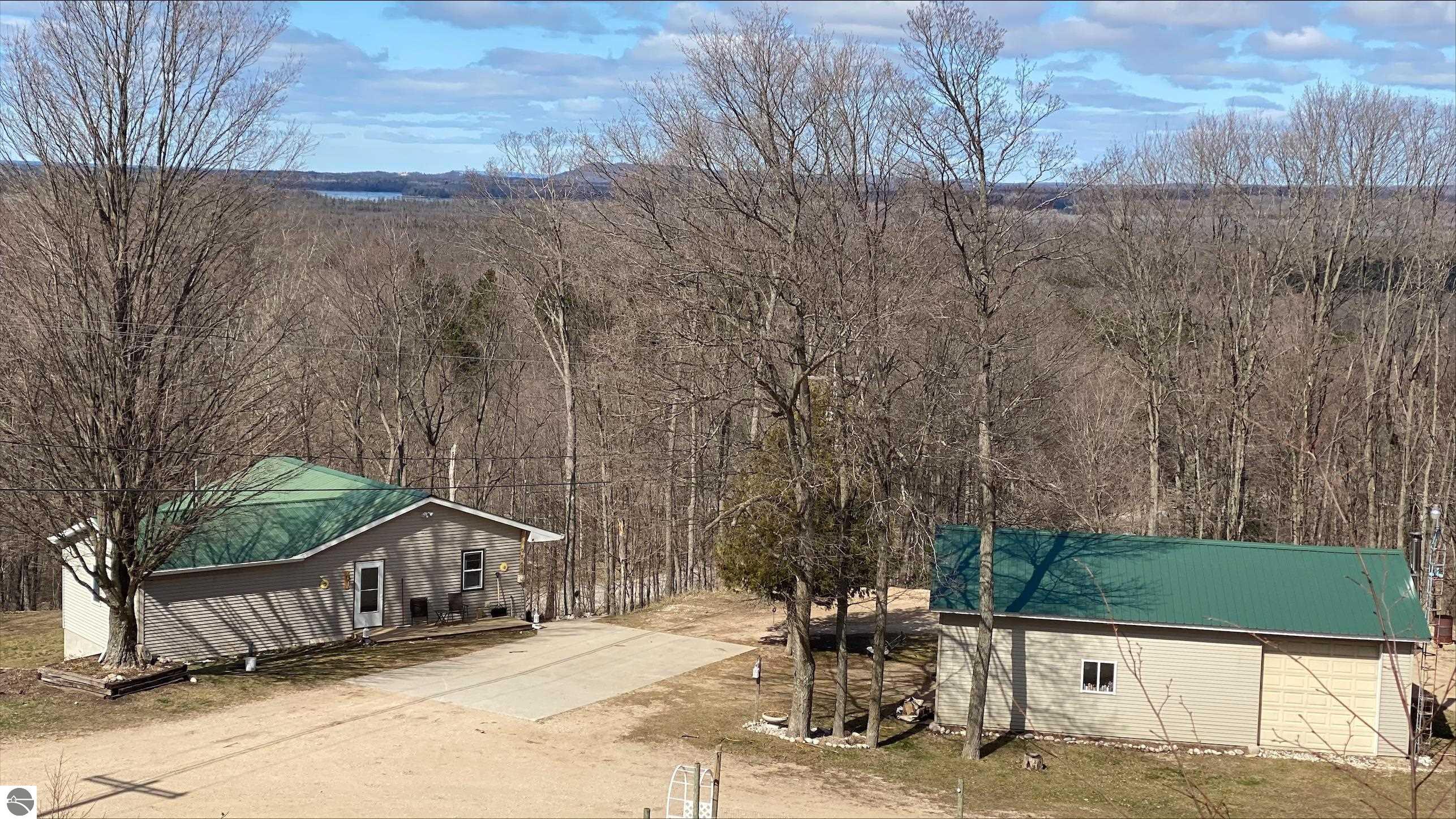 Beulah home and separate pole building are pictured from above with mature trees and distant views.