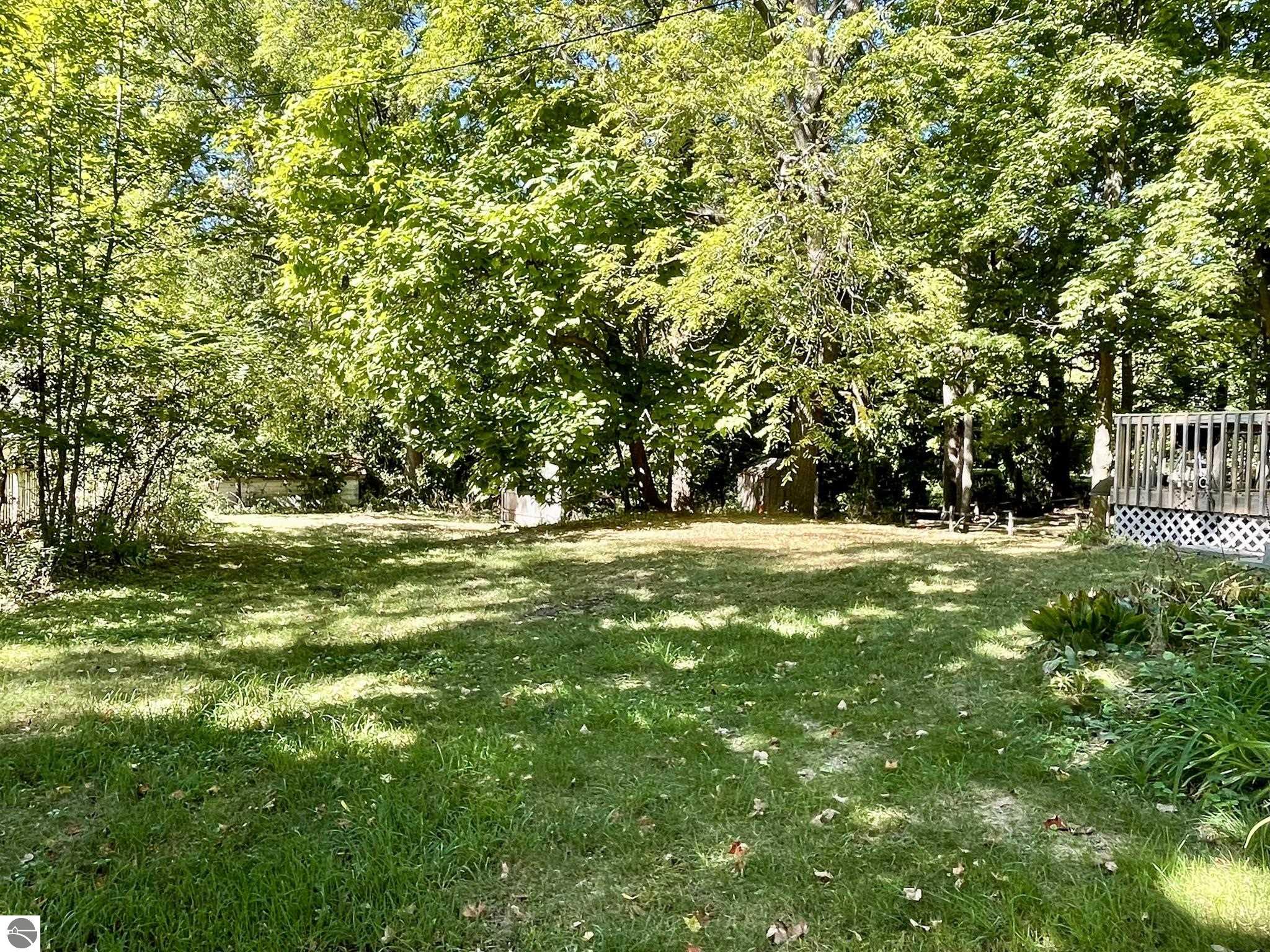 Benzonia Village Farmhouse image of of the backyard and a portion of the deck overlooking green grass and shade trees. 