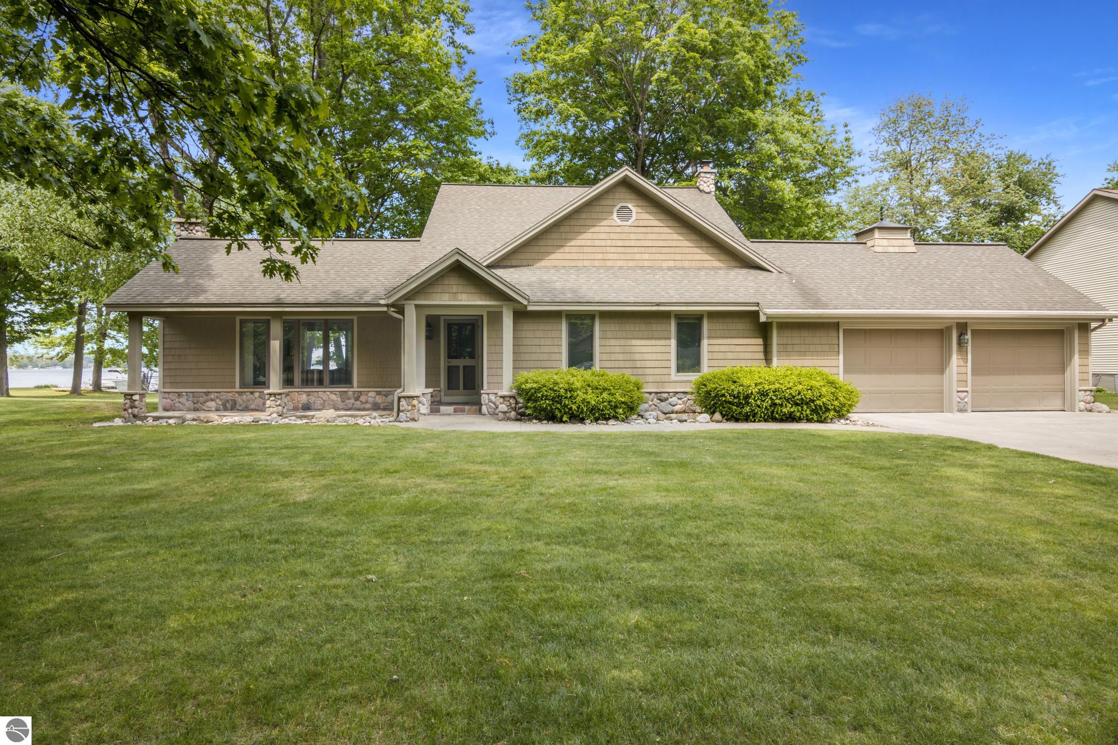 Image for Big Platte Lake waterfront is a photo of the front of the house on Birch Drive with a covered front porch, two-stall garage, paved driveway and lawn.